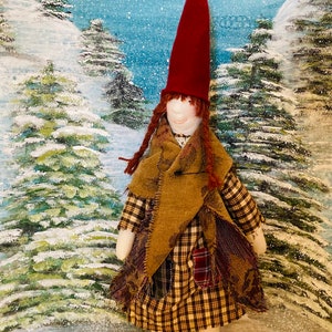 May include: A handmade rag doll wearing a red hat, brown hair, and a plaid dress. The doll is standing in front of a snowy winter scene.