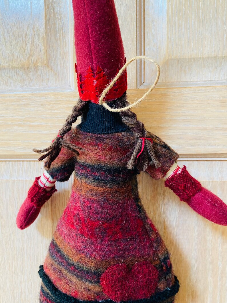 Peut inclure: Poup&eacute;e artisanale avec un grand chapeau en feutre bordeaux et une robe assortie. La poup&eacute;e a des tresses brunes, des moufles rouges et un d&eacute;tail en forme de c&oelig;ur sur la robe. Une ficelle de jute est attach&eacute;e au chapeau pour l'accrocher.