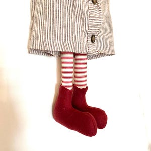 May include: A fabric doll with a striped dress and red and white striped legs. The doll's feet are a solid, deep red colour. The dress has a button closure.