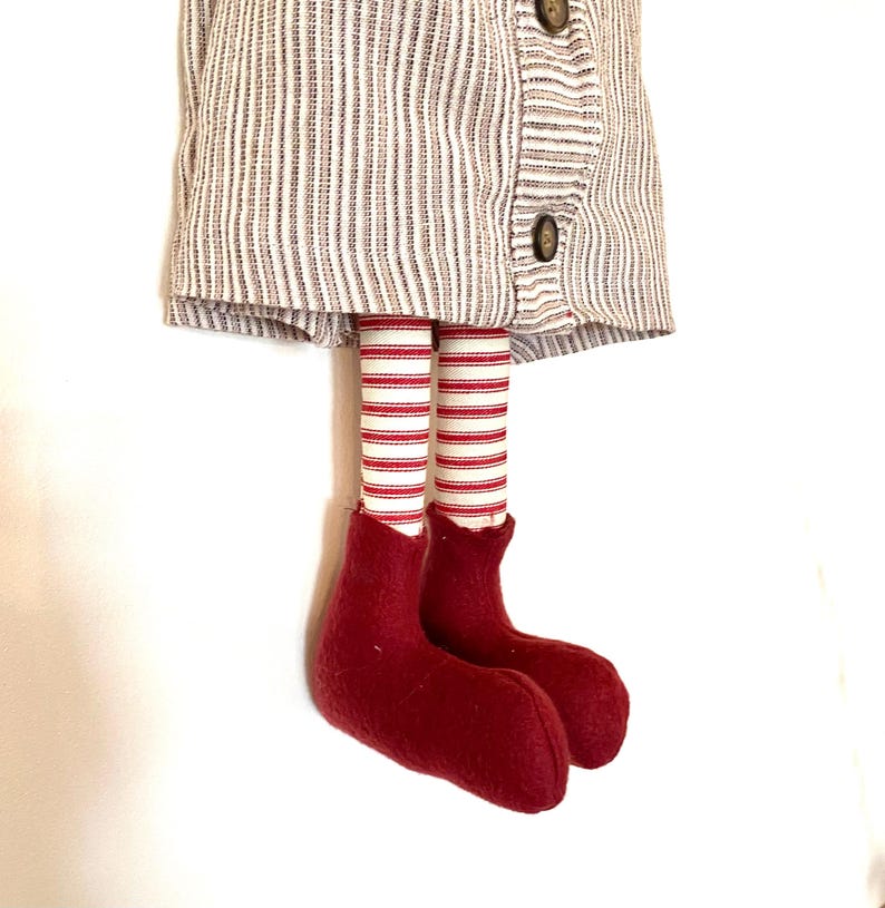 May include: A fabric doll with a striped dress and red and white striped legs. The doll's feet are a solid, deep red colour. The dress has a button closure.