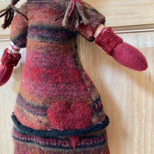 Peut inclure: Poup&eacute;e faite &agrave; la main avec une application de c&oelig;ur rouge sur le devant. La poup&eacute;e porte une robe ray&eacute;e dans les tons de rouge, marron et noir, avec des mitaines assorties. La poup&eacute;e a des cheveux bruns tress&eacute;s et des jambes ray&eacute;es.