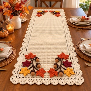 Peut inclure: Un chemin de table rectangulaire en crochet de couleur crème avec un bord festonné et une texture en grille. Le chemin est décoré aux deux extrémités par des appliqués de feuilles d'automne en crochet dans des tons rouge, orange et jaune, ainsi que des glands marron.