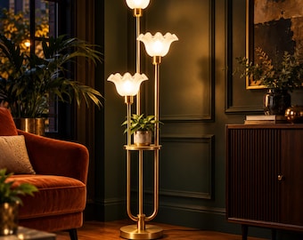 May include: A gold-toned floor lamp featuring three vertical poles of varying heights, each topped with a white, ruffled, bell-shaped glass shade. A circular shelf is integrated into the center of the lamp structure, holding a small potted plant.