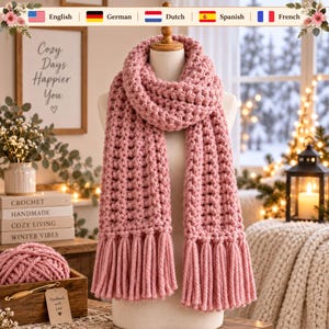 May include: A chunky knit scarf in a dusty rose color, featuring a thick, textured stitch pattern and long, twisted fringe tassels at both ends. The scarf is displayed on a neutral-toned mannequin, showcasing its soft, voluminous yarn construction.