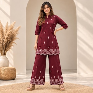 May include: A deep maroon tunic and wide-leg trousers set featuring white floral embroidery. The tunic has a notched neckline and three-quarter length sleeves. Both the tunic hem and the trouser cuffs are finished with a white scalloped edge.