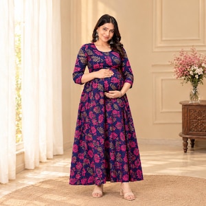 May include: A floor-length navy blue dress featuring a vibrant pink and gold leaf pattern, three-quarter length sleeves, and a round neckline. The garment has a fitted bodice that transitions into a full, flowing skirt with a consistent floral print.