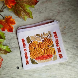 May include: White zippered pouch with embroidered pumpkins and leaves. The text reads "Spice fills the air. The smell of pumpkin."