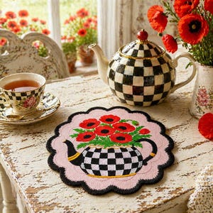 May include: A charming tea setting featuring a black and white checkered teapot, teacup, and saucer. A pink placemat with a teapot design filled with red poppies sits on a distressed white table. A vase of red poppies adds a pop of color.