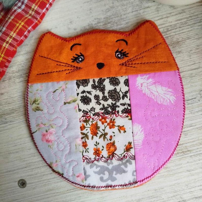 Pu&ograve; includere: Un sottobicchiere fatto a mano a forma di gatto arancione con un motivo floreale. Il sottobicchiere &egrave; realizzato con diversi tessuti e ha una texture trapuntata.