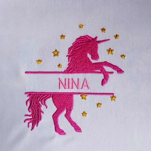Può includere: Design ricamato con un unicorno rosa con il nome "NINA" in uno striscione. Stelle dorate circondano l'unicorno su sfondo bianco. L'unicorno si impenna sulle zampe posteriori.