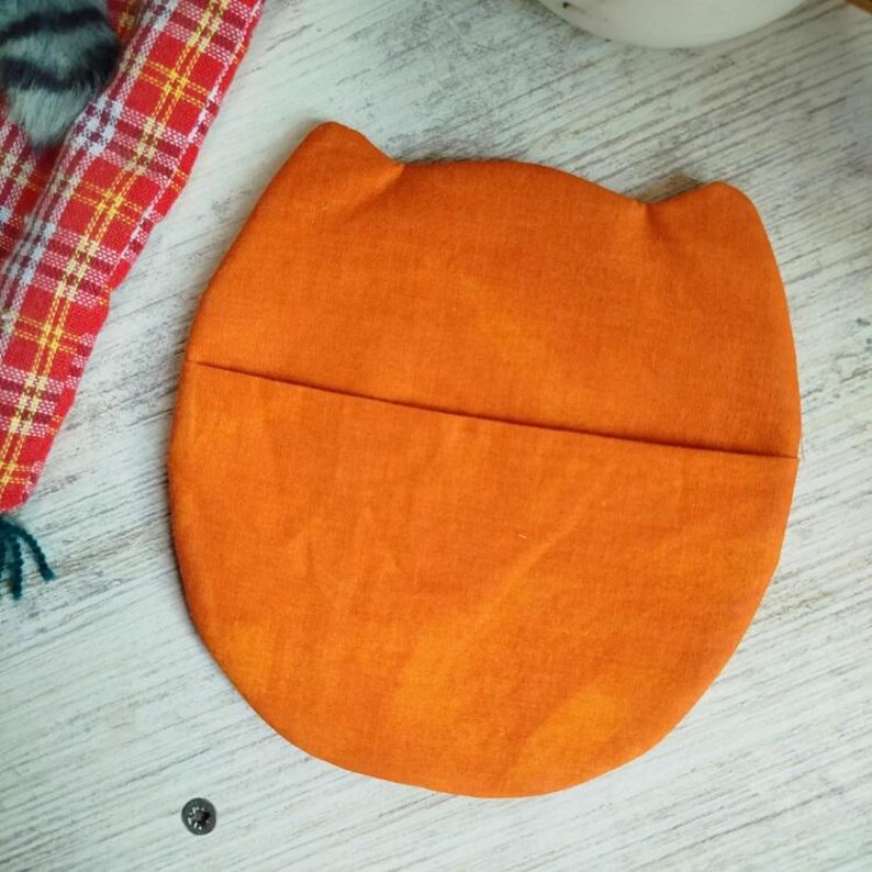 Pu&ograve; includere: Sottobicchiere in tessuto arancione a forma di gatto con una tasca sul retro.