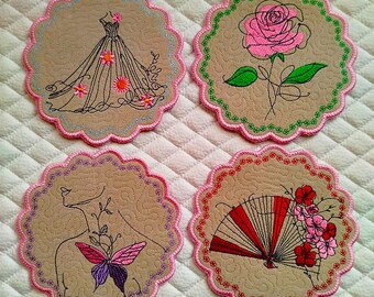 May include: Four beige fabric coasters with scalloped edges. Each coaster features a different embroidered design: a gown, a rose, a butterfly, and a fan with flowers. The edges are trimmed with pink and silver thread.