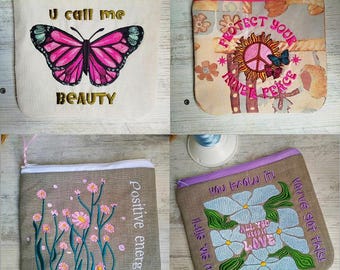 Può includere: Quattro diverse pochette con cerniera con disegni ricamati. La prima pochette è bianca con un ricamo di farfalla rosa e il testo "U call me BEAUTY". La seconda pochette è beige con un segno di pace e il testo "PROTECT YOUR INNER PEACE". La terza pochette è beige con fiori rosa e il testo "Positive energy". La quarta pochette è beige con fiori blu e il testo "You know it! You've got this! All you need is LOVE. I like the way you..."