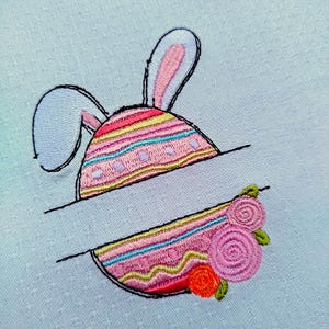 Peut inclure: Broderie d'un œuf de Pâques avec des oreilles de lapin, orné de rayures roses, jaunes et bleues. L'œuf est divisé avec un espace vide pour la personnalisation, et orné de roses roses et d'une fleur orange. Le motif est posé sur un fond bleu clair texturé.