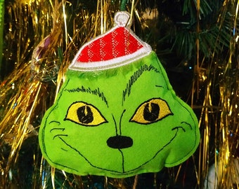May include: Green felt Christmas bauble with a stitched Grinch face, wearing a red and white Santa hat.