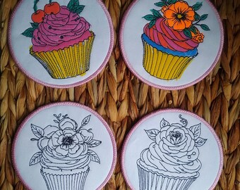 May include: Four round iron-on patches with pink stitching. Each patch features a cupcake with different designs. One cupcake has cherries on top, another has a flower, and two are outlined in black.