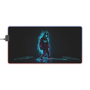 Peut inclure: Un tapis de souris de jeu rectangulaire noir avec un motif central bleu néon et violet représentant une silhouette à capuche portant un masque stylisé. Le design inclut des traînées lumineuses et un petit boîtier de commande noir sur le côté.