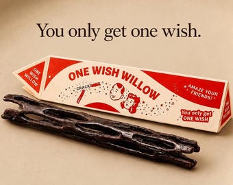 Könnte beinhalten: Ein dunkelbrauner, poröser, zylindrischer Holzstab vor einer dreieckigen Pappschachtel. Die Schachtel ist cremefarben und rot mit dem aufgedruckten Text 'ONE WISH WILLOW', 'You only get one wish' und 'AMAZE YOUR FRIENDS!' auf der Vorderseite.