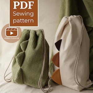 May include: A PDF sewing pattern for two drawstring bags. One bag is made of olive green corduroy fabric, and the other is made of off-white canvas. Both bags feature three triangular fabric spikes along the side and include a video tutorial.