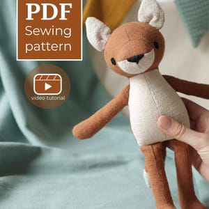 May include: A brown and cream-colored fabric fox doll with black embroidered eyes and nose. The image includes a brown square graphic with the white text PDF Sewing pattern and a circular icon with the text video tutorial.