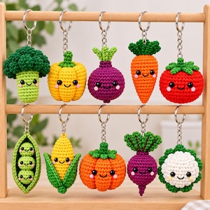 May include: A collection of ten crocheted vegetable keychains hanging from a wooden rack. The set includes a broccoli, yellow pepper, purple beet, carrot, tomato, pea pod, corn, orange pumpkin, another purple beet, and a white cauliflower.