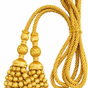 May include: A pair of gold-colored curtain tiebacks featuring two large tassels with spherical, textured heads and multiple dangling, rounded beads. The tassels are connected by long, thick, twisted gold cords that loop together.