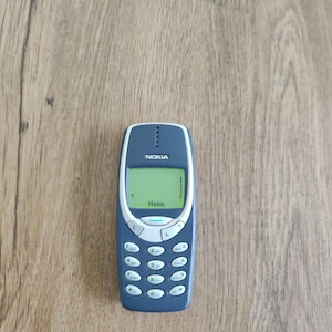 May include: A dark blue Nokia mobile phone with a light green screen displaying the word Menu. The device features a standard numeric keypad with white buttons, a central navigation bar, and a speaker grill located above the Nokia brand logo.