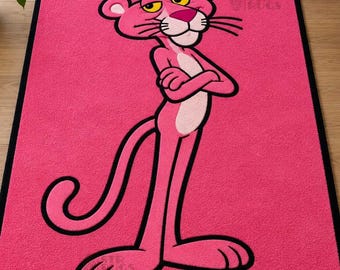 May include: A rectangular area rug featuring a vibrant pink background and a black border. The center displays a large, full-body illustration of the Pink Panther character with arms crossed, rendered in shades of pink with a light pink chest.