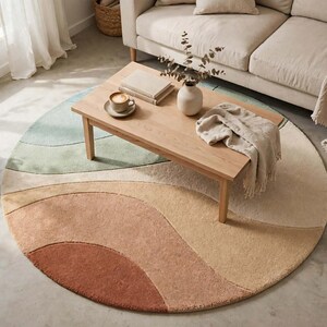 May include: A round area rug featuring a layered, abstract wave pattern in shades of terracotta, beige, cream, and sage green. The rug has a soft, textured pile and is positioned under a light-toned wooden coffee table in a living space.