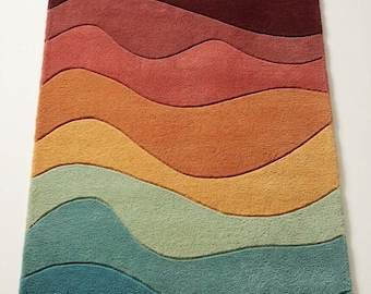 May include: A rectangular area rug featuring a series of horizontal, undulating wave patterns in a gradient of colors, transitioning from deep burgundy at the top through shades of red, orange, yellow, and sage green to dark teal at the bottom.