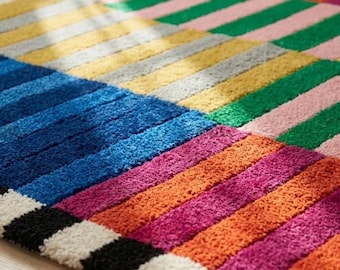 May include: A rectangular area rug featuring a vibrant, multi-colored striped pattern. The design consists of horizontal bands in shades of blue, yellow, green, pink, orange, magenta, black, and white, with a textured, tufted pile construction.