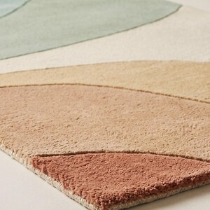 May include: A rectangular area rug featuring a tufted texture with abstract, curved, layered shapes in a palette of muted blue, sage green, cream, beige, tan, and terracotta orange, arranged in a flowing, landscape-inspired pattern.