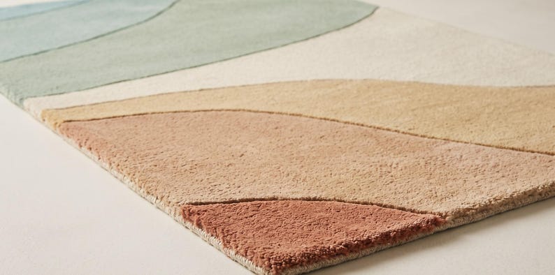 May include: A rectangular area rug featuring a tufted texture with abstract, curved, layered shapes in a palette of muted blue, sage green, cream, beige, tan, and terracotta orange, arranged in a flowing, landscape-inspired pattern.