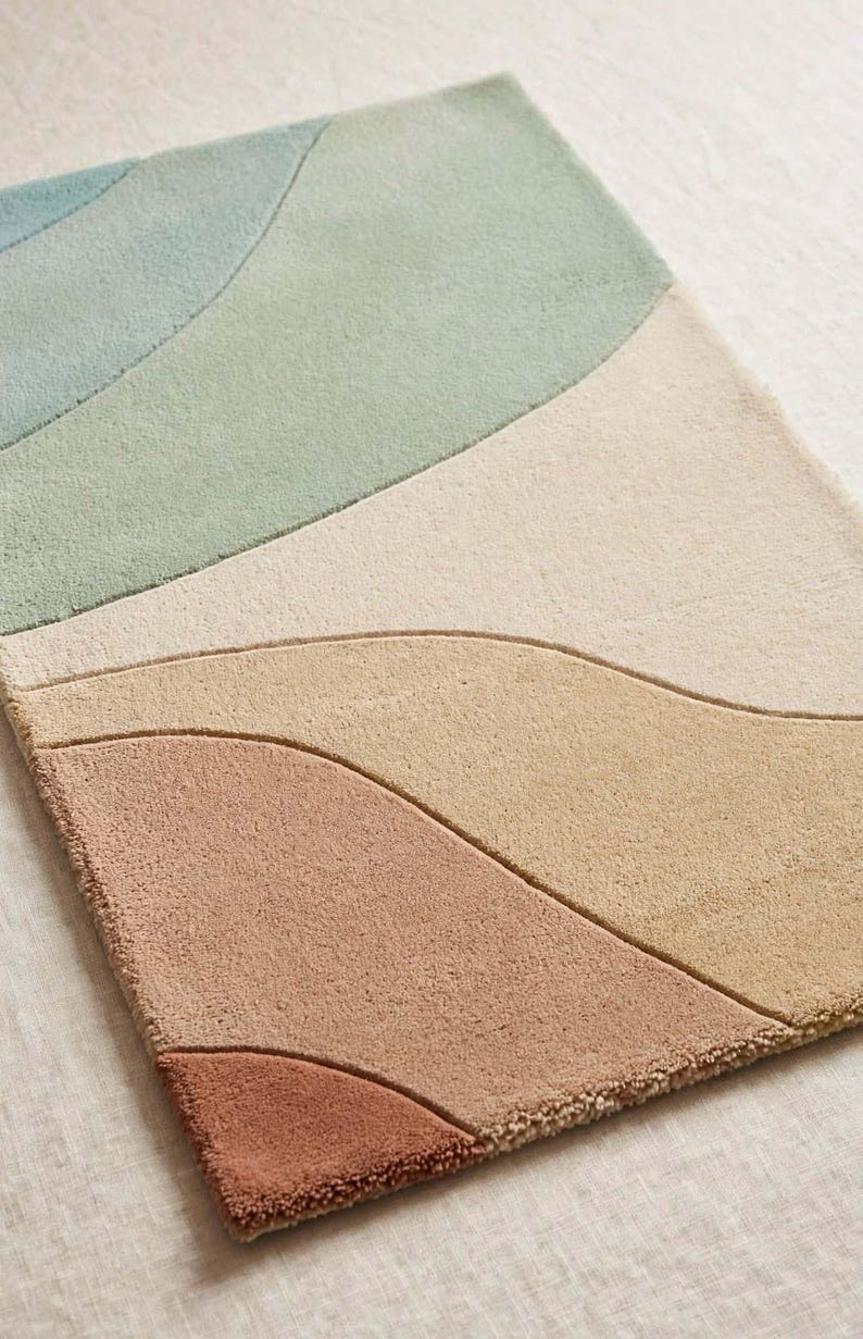 May include: A rectangular area rug featuring a tufted texture with abstract, curved, wave-like sections in muted shades of sage green, light blue, cream, beige, terracotta, and dark rust, separated by recessed lines in the pile.