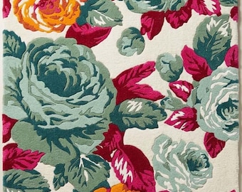May include: A rectangular area rug featuring a dense floral pattern on an off-white background. The design consists of large, tufted roses in shades of teal, magenta, and orange, interspersed with green leaves and smaller floral buds throughout.