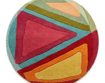 May include: A circular rug featuring a geometric pattern of overlapping shapes in shades of magenta, teal, olive green, orange, yellow, and peach. The design consists of thick, tufted lines creating distinct triangular and angular sections.