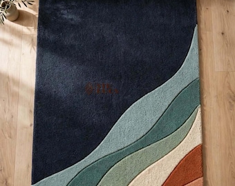 May include: A rectangular area rug featuring a large dark navy blue section contrasted by flowing, wave-like bands of sage green, cream, and terracotta orange. The rug has a thick, plush texture and is positioned on a light-colored wooden floor.