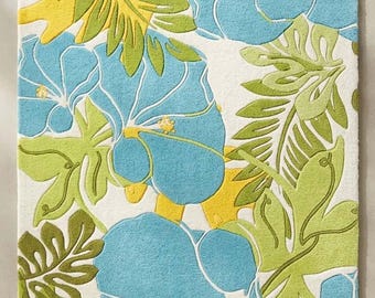 May include: A rectangular area rug featuring a white background with a pattern of large light blue hibiscus flowers, yellow accents, and various shades of green tropical leaves. The bottom right corner displays a small logo reading STR RUGS.
