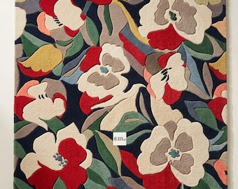 May include: A rectangular area rug featuring a dense, multi-colored floral pattern against a dark navy blue background. The design includes stylized flowers in shades of red, cream, yellow, and grey, interspersed with green leaves. A small white label with the text "SIE RUGS" is visible near the center.