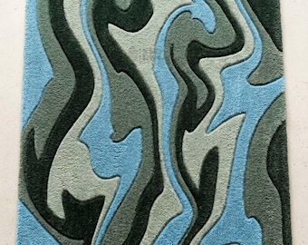 May include: A rectangular area rug featuring a high-pile, tufted texture with an abstract, flowing pattern of wavy, organic shapes. The design consists of layered, interlocking color blocks in shades of sky blue, sage green, and dark charcoal.