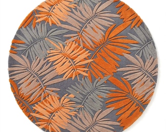 May include: A circular rug featuring a repeating pattern of palm leaves in shades of bright orange, muted tan, and dark gray. The design consists of overlapping botanical shapes with a textured, tufted surface that creates a distinct visual depth.