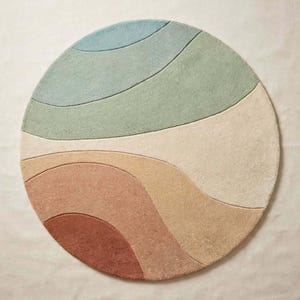 May include: A circular area rug featuring a series of curved, wave-like sections in a palette of muted blue, sage green, cream, soft yellow, peach, and terracotta. The rug has a textured, tufted surface with distinct carved lines.