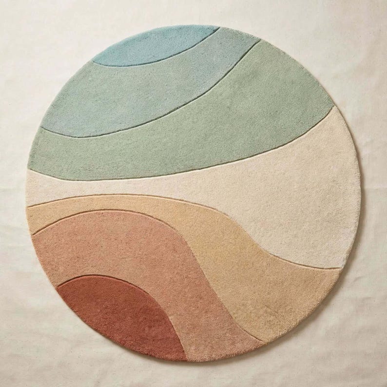 May include: A circular area rug featuring a series of curved, wave-like sections in a palette of muted blue, sage green, cream, soft yellow, peach, and terracotta. The rug has a textured, tufted surface with distinct carved lines.