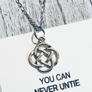 Puede incluir: Un collar plateado con un colgante de nudo celta. El colgante tiene un dise&ntilde;o de tr&eacute;bol de cuatro hojas. El collar est&aacute; sobre una tarjeta blanca con el texto "YOU CAN NEVER UNTIE".
