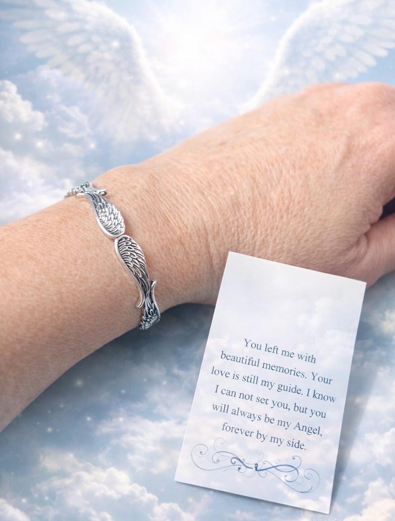 Puede incluir: Pulsera plateada con alas de &aacute;ngel. La pulsera se lleva en la mu&ntilde;eca, con una tarjeta que dice "You left me with beautiful memories. Your love is still my guide..." sobre un fondo de cielo nublado.