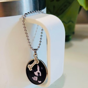 May include: A silver chain necklace with a round pendant featuring a black and white dog silhouette and a bone charm. The pendant has the text "THE NORTH FACE" printed on it.