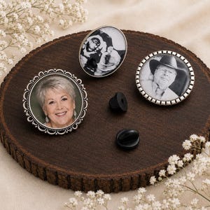 May include: Three circular and oval photo pins featuring black and white portraits of individuals. The pins have silver-toned metal frames with decorative edges and include two black rubber clutch backings for secure attachment to clothing.