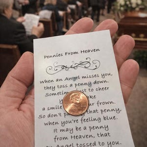 May include: A penny rests on a card with the text "Pennies From Heaven." The card's message is a poem about finding comfort in a penny. The background shows a funeral service.