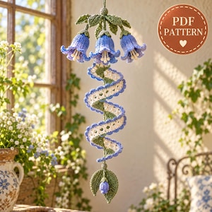 May include: A hanging crochet decoration featuring three blue bell-shaped flowers with green leaves at the top, connected to a spiraling white and blue ribbon-like structure, ending with a small blue bud and green leaves. Text reads PDF PATTERN.