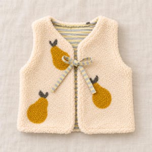 Könnte beinhalten: Eine cremefarbene Sherpa-Fleece-Weste mit drei texturierten, senfgelben Birnen-Applikationen mit dunkelgrauen Stielen. Die Weste verfügt über einen Verschluss zum Binden aus hellblau-weiß gestreiftem Band und ein passendes gestreiftes Innenfutter.